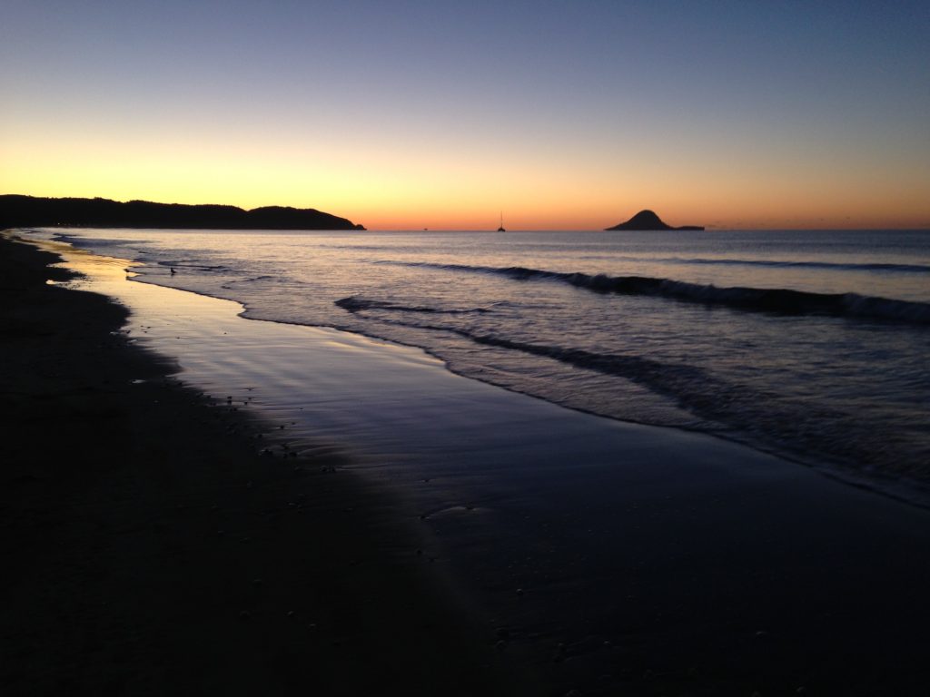 Waves roll in as the sun sets at Ōhope Beach, with Whale Island in the far background.