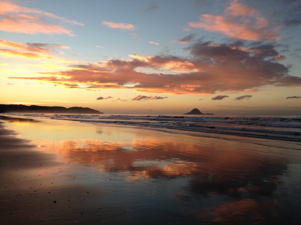 Clouds reflect off wet sand just before sunset at Ōhope Beach.